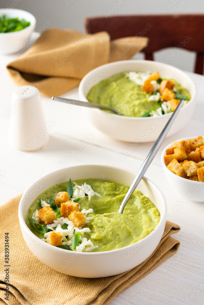 Healthy delicious broccoli and cucumber cream puree soup with mozzarella, green onions and croutons, bowl of soup on a white table Healthy delicious broccoli and cucumber cream puree soup with mozzarella, green onions and croutons, bowl of soup on a white table