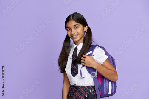 Happy smiling indian preteen girl, latin kid schoolgirl with ponytails wears uniform holding backpack standing isolated on lilac violet background looking at camera, back to school concept, portrait. photo