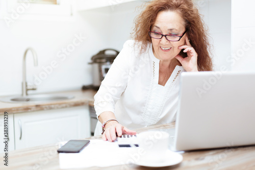 Retired woman resting on the kitchen table. She is using a calculator and checking bills. © Alfredo López