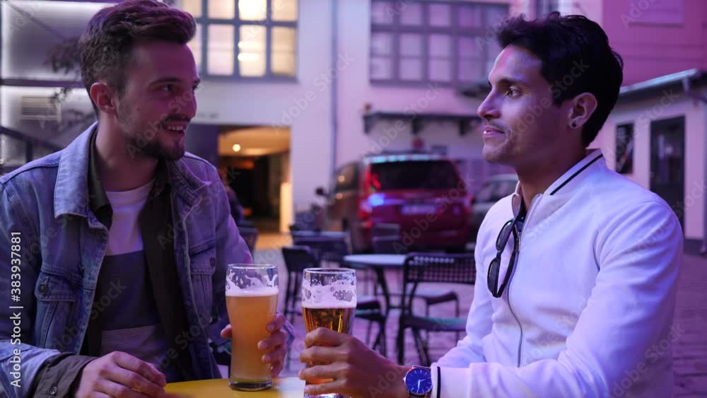 Hanging out two young guys friends in street bar drink alcohol beer from glass communicating in neon lights