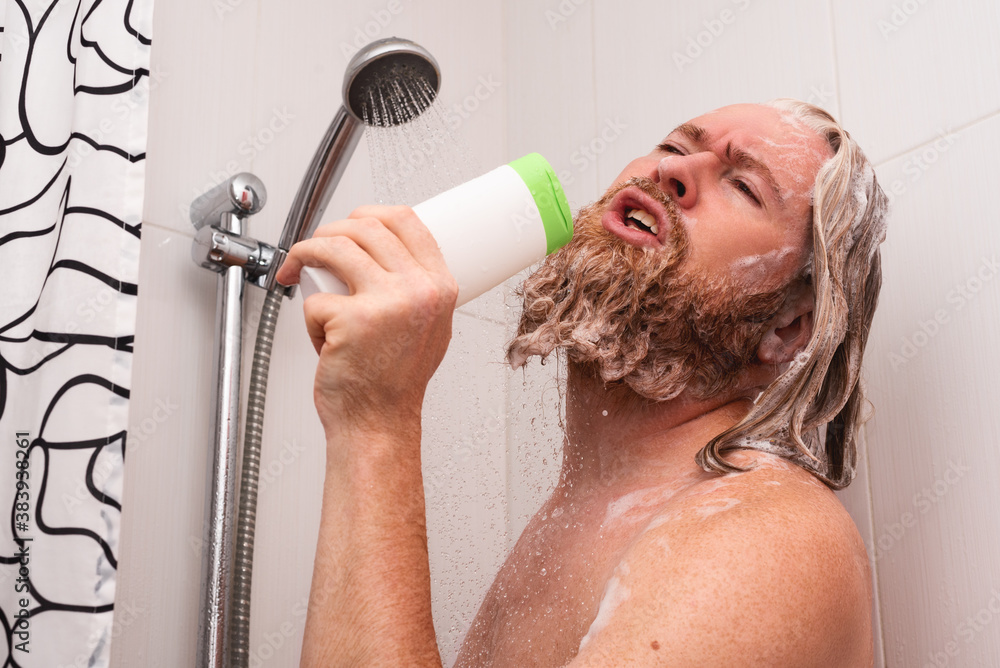Handsome bearded man singing while taking shower at home using shampoo bottle instead of microphone. Happy caucasian guy sings with facial expression enjoying life.