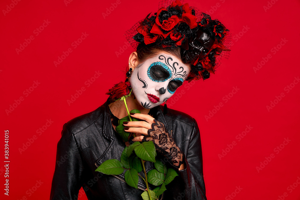 Romantic dead gir with sugar skull makeup with a wreath of flowers on her head and skull, wearth black gloves holding red rose isolated on red background. concept of Halloween or Calavera Catrina Romantic dead gir with sugar skull makeup with a wreath of flowers on her head and skull, wearth black gloves holding red rose isolated on red background. concept of Halloween or Calavera Catrina