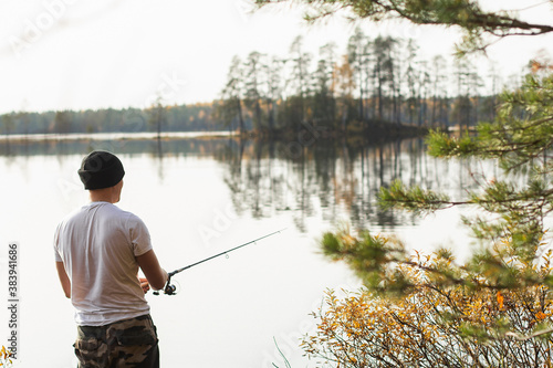 Fisherman Fishing on spinning on beautiful morning autumn lake with conifeur forest banks.