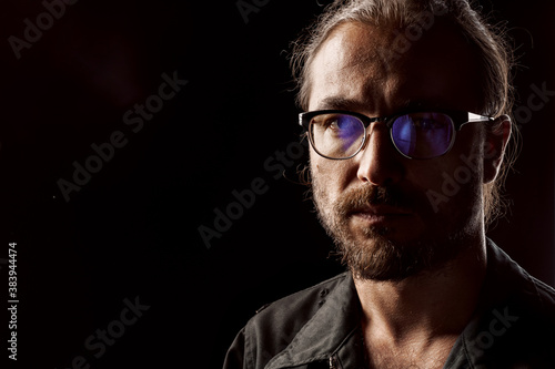 Dark studio portrait of a middle-aged man with beard in glasses