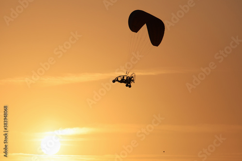 Paraglider flying above the sun, under the orange rays of the setting sun