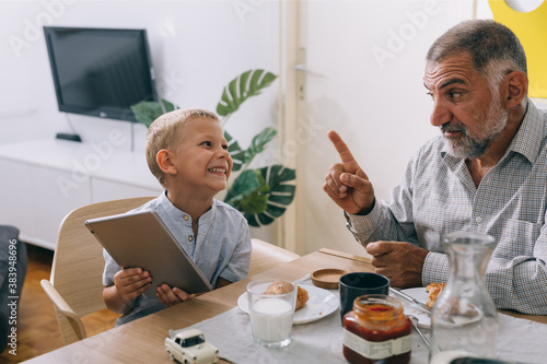 grandfather and grandson having breakfast at home, boy using tablet computer