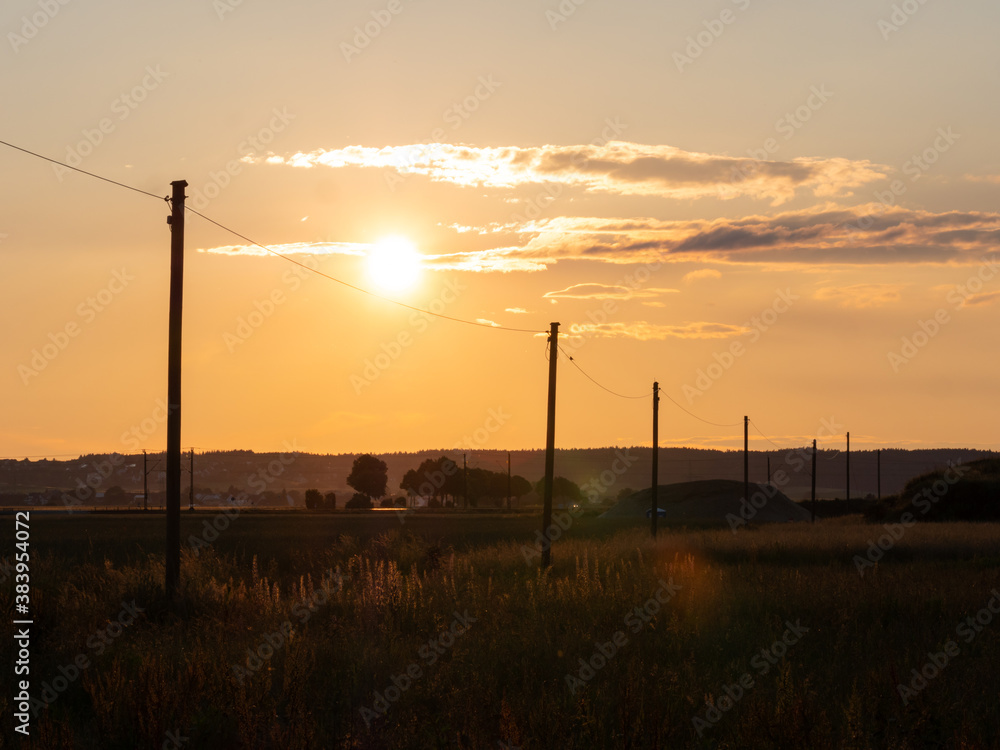 Sunset with the silhouette of high voltahe power posts. Beautiful natural landscape in the summer time