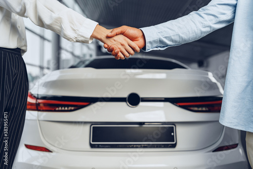 Car seller and buyer handshake at car dealership against a new car