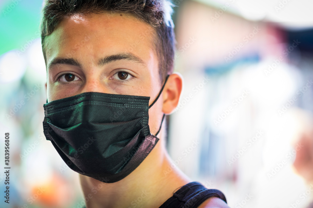 Portrait of a handsome brown-eyed teenage boy wearing a black surgical mask due to covid coronavirus infection Portrait of a handsome brown-eyed teenage boy wearing a black surgical mask due to covid coronavirus infection