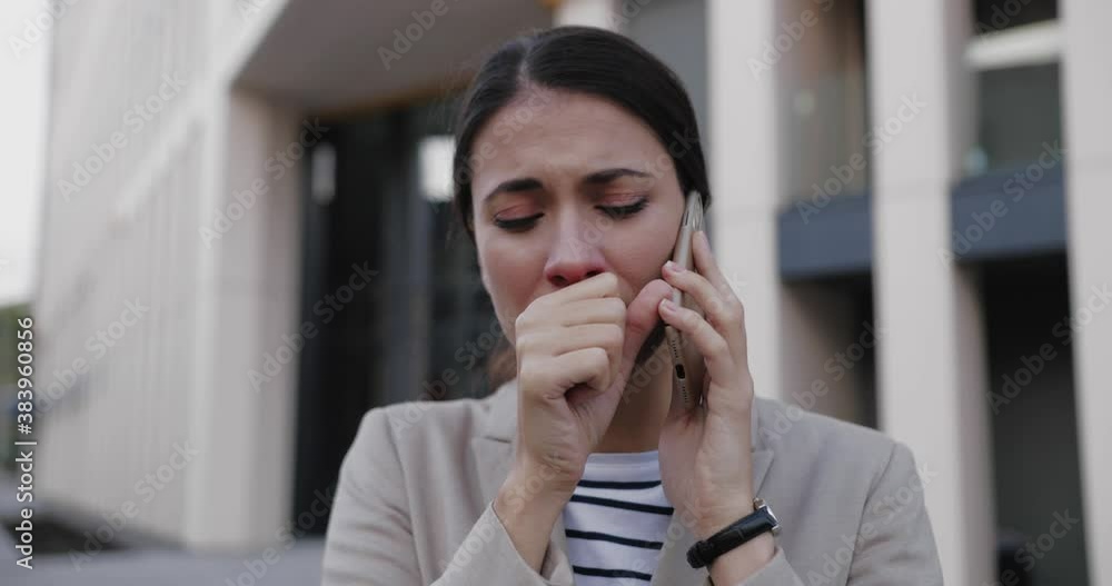 Close up of young unwell Caucasian woman worker standing in city and coughing while talking on smartphone. Portrait of sick beautiful female with cold calling on cellphone outdoor. Health concept Close up of young unwell Caucasian woman worker standing in city and coughing while talking on smartphone. Portrait of sick beautiful female with cold calling on cellphone outdoor. Health concept