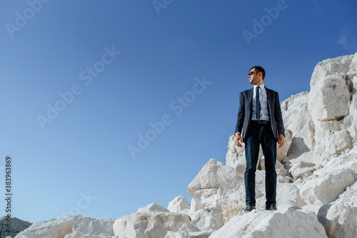 man in classic clothes, jacket, tie and glasses is posing on the mountain.