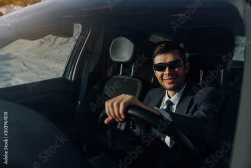 man businessman in a jacket, shirt, tie and sunglasses is driving a car. © Med Photo Studio