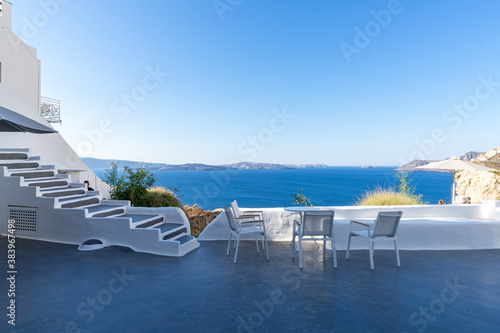 Four white chairs with white table on the white terrace with blue sea and caldera view on a sunny day  without people. Oia  Santorini island  Greece