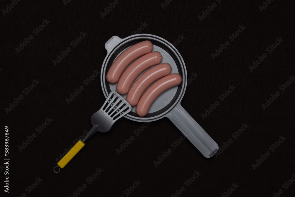 Toy sausages on a frying pan on a wooden background Toy sausages on a frying pan on a wooden background