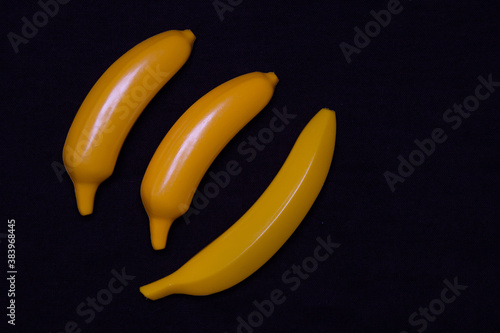 Three bananas on a dark background. Plastic toy