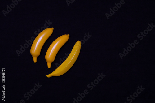 Three bananas on a dark background. Plastic toy