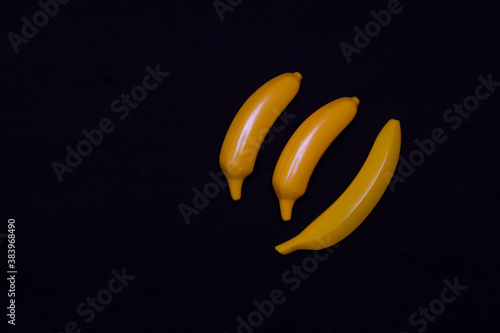 Three bananas on a dark background. Plastic toy