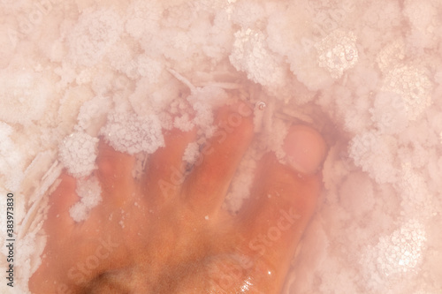 Man leg foot fingers close-up in pink salt flakes top view under pink water surface. Healthy spa procedures