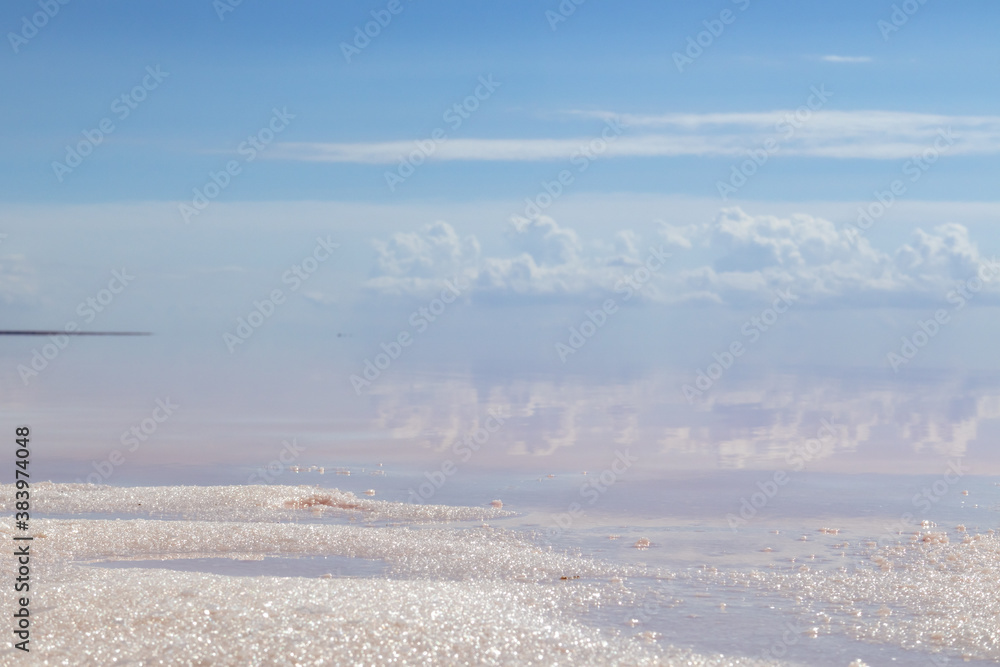 Salt sand crystals close-up shining on lake coast with pink water surface and reflection of clouds and blue sky. Syvash or Sivash, the Putrid Sea or Rotten Sea, Ukraine Salt sand crystals close-up shining on lake coast with pink water surface and reflection of clouds and blue sky. Syvash or Sivash, the Putrid Sea or Rotten Sea, Ukraine
