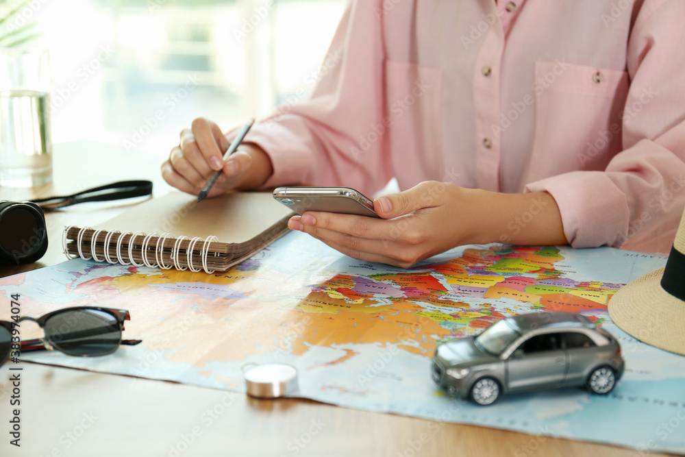 Fototapeta premium Woman with world map and smartphone planning trip at wooden table, closeup