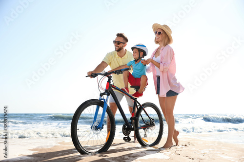 Happy parents teaching son to ride bicycle on sandy beach near sea