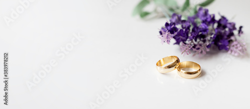 Purple flowers and two golden wedding rings on white background.	