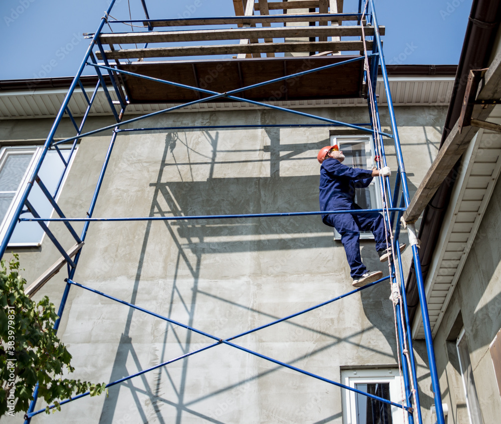Construction of houses. A worker climbs the scaffolding to the roof of the house.