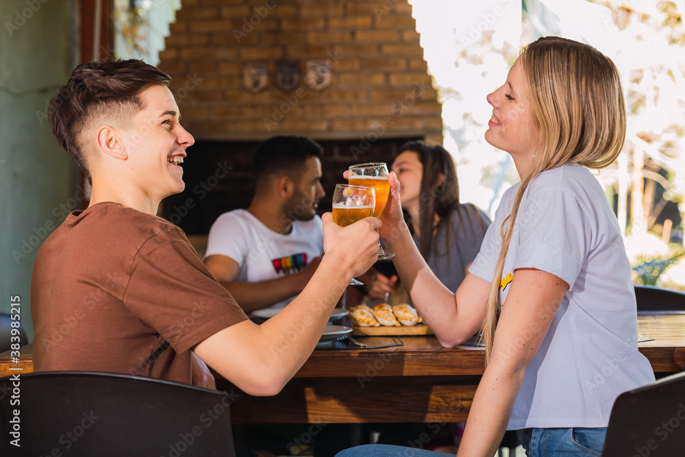 Couple toasting beer at outdoor restaurant bar.  Lifestyle concept with happy people having fun together.  Focus on the couple in front.