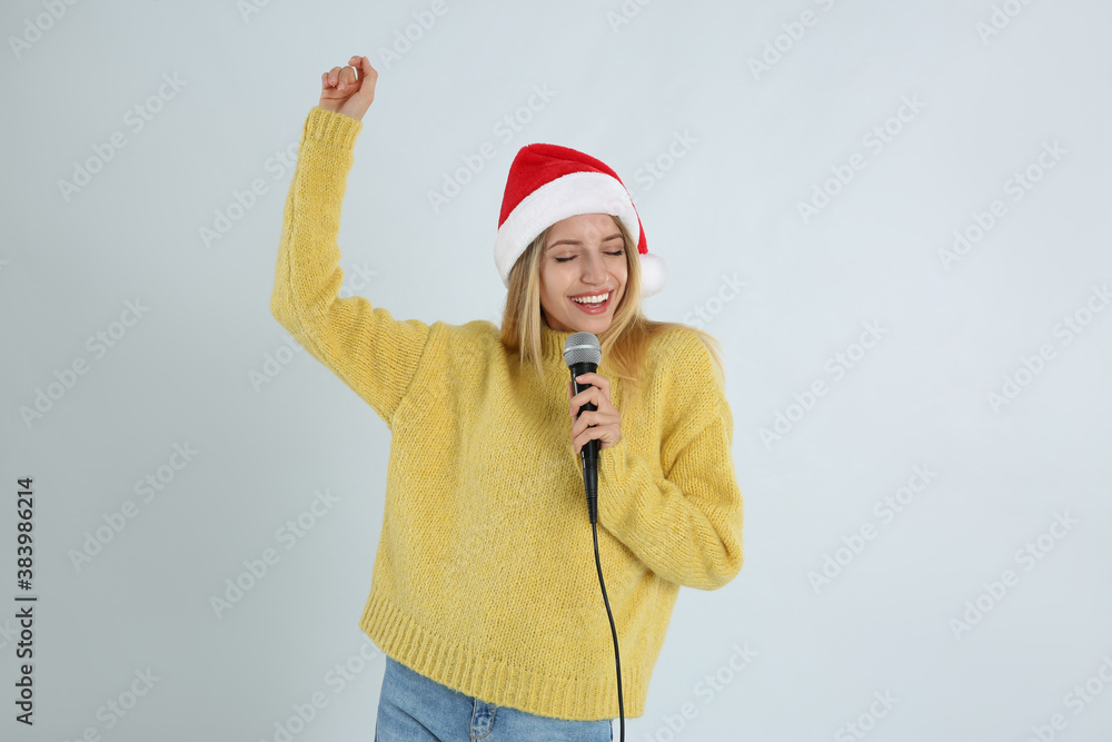Emotional woman in Santa Claus hat singing with microphone on light grey background. Christmas music Emotional woman in Santa Claus hat singing with microphone on light grey background. Christmas music
