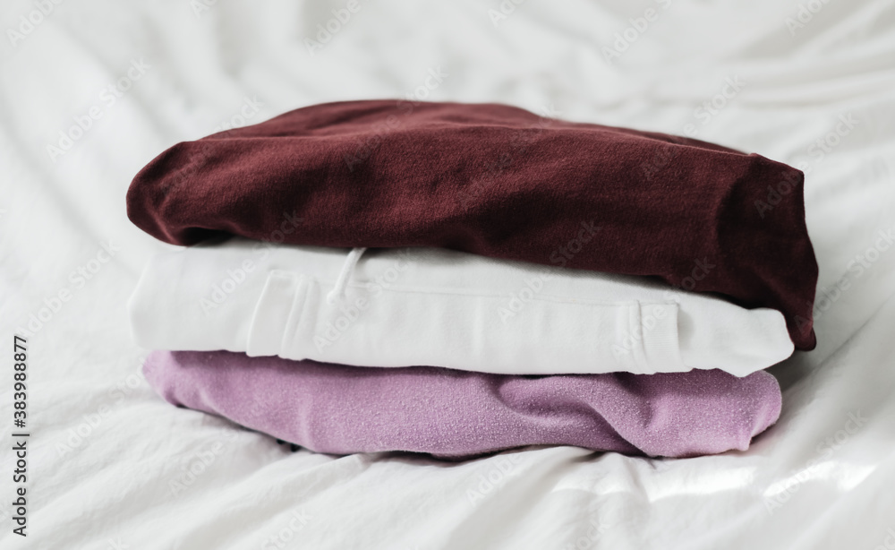Stack of multicolored clothes on a white bed from wardrobe. 