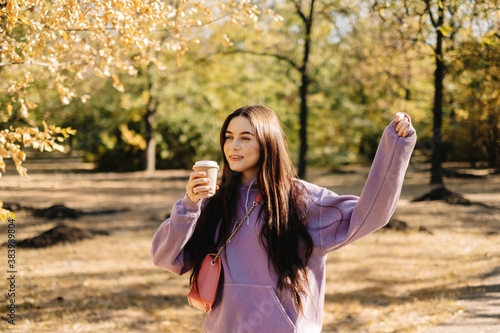 Beautiful young woman having fun, drinking coffee and enjoying autumn weather in the park. Woman walking in the autumn park.