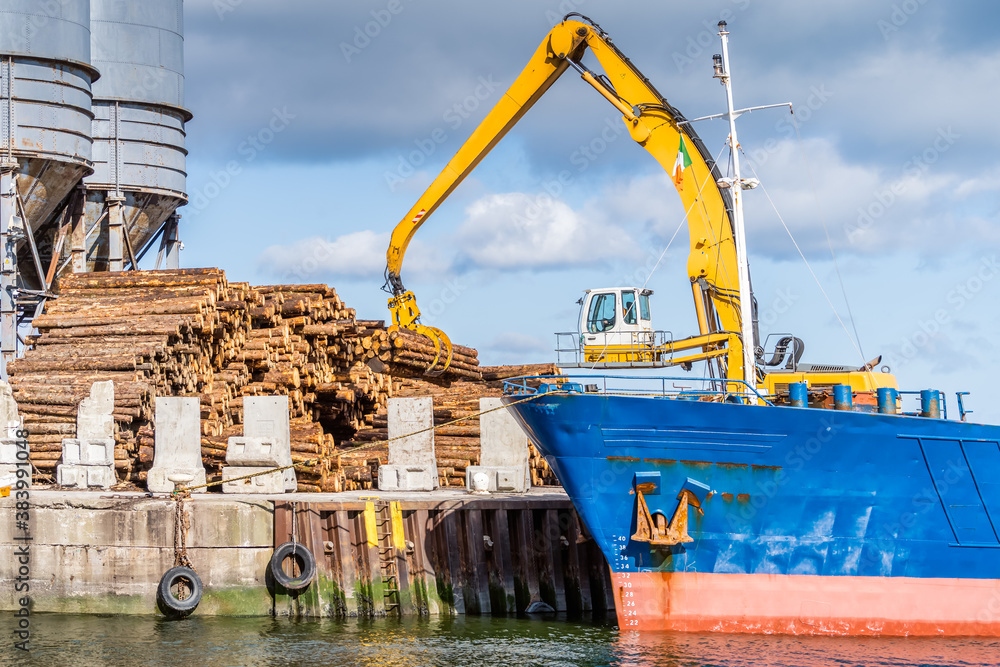 Crane with wood logs gripple loading timber on cargo ship for export in Wicklow commercial port. Transport industry in Ireland
