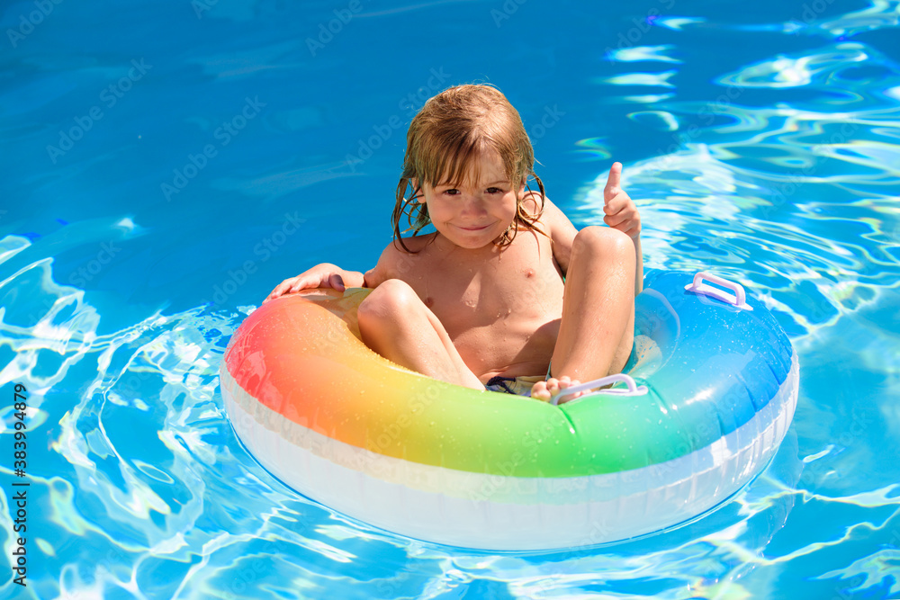 Cute funny little toddler child boy with thumb up in a colorful swimming suit and sunglasses relaxing. Kid with toy ring floating in a pool having fun during summer vacation in a tropical resort.