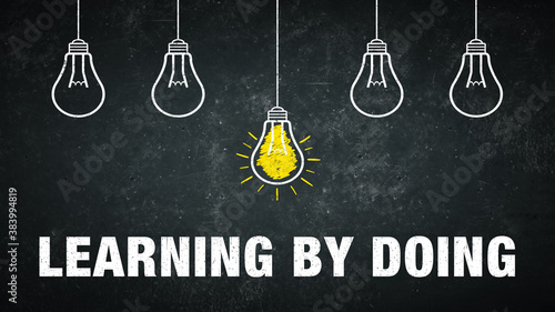 фотографія Phrase „learning by doing“ on a rustic background with 5 light bulbs