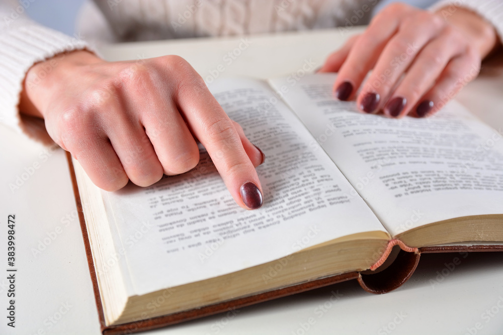 Fototapeta premium Female hands with brown nails polish color and finger on an open book. Manicure and beauty concept