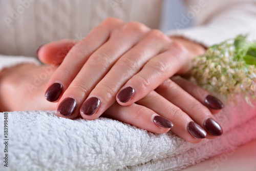 Female hands with brown nails polish color on a towel in a beauty salon on a white desk with decoration. Manicure and beauty concept