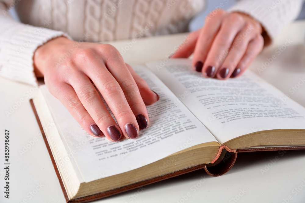 Woman hand on an open book and brown gel nails polish on fingers. Manicure and beauty concept Woman hand on an open book and brown gel nails polish on fingers. Manicure and beauty concept