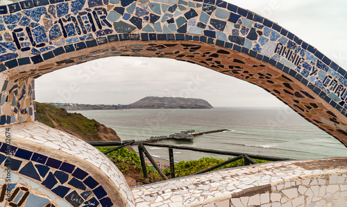 Miraflores, Peru - December 4, 2008: Parque del Amor, Love Park. Gray-green Pacific Ocean with Pier and mountainous coastline visible under art faience bow of stone. Some green foliage.  photo