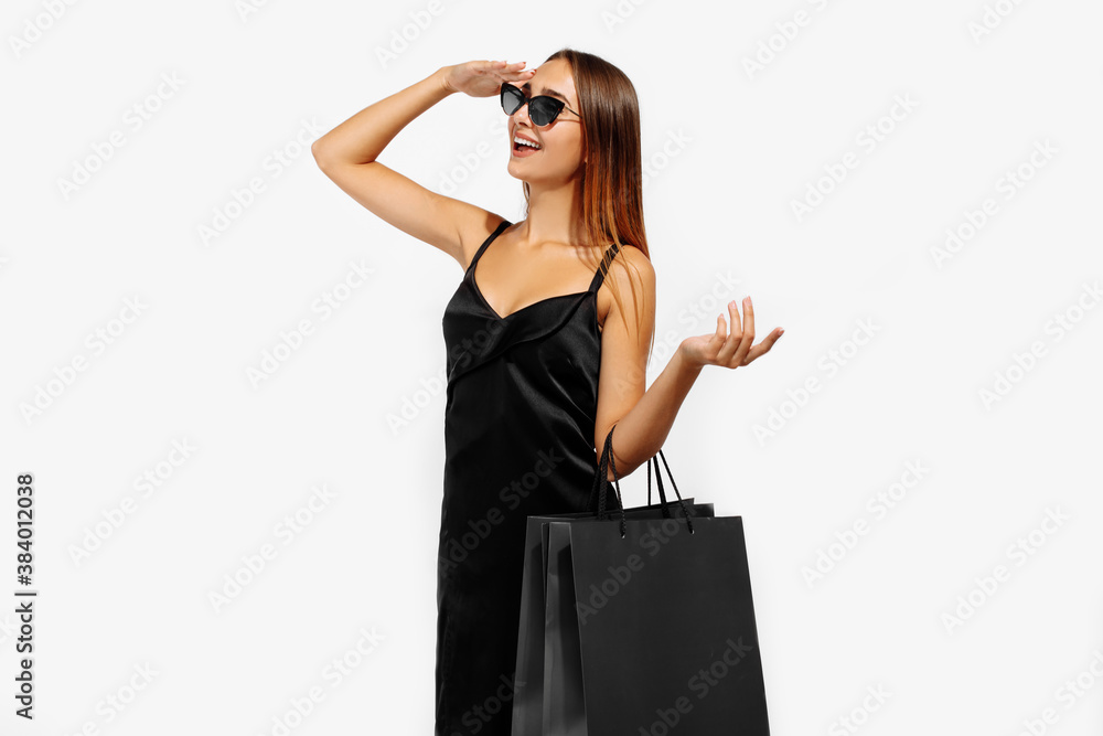 Beautiful young woman in sunglasses, in a black dress holds bags and looks into the distance on a white background, Black Friday, shopping Beautiful young woman in sunglasses, in a black dress holds bags and looks into the distance on a white background, Black Friday, shopping
