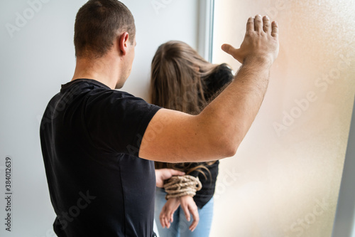 Back view on unknown man beating woman in hall of hotel or house - Female or minor girl with tied hands tortured by aggressive male person - Human rights kidnapping sex trafficking violence concept