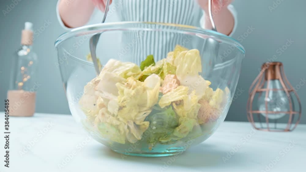Mixing with forks a freshly made green Caesar salad into a glass bowl