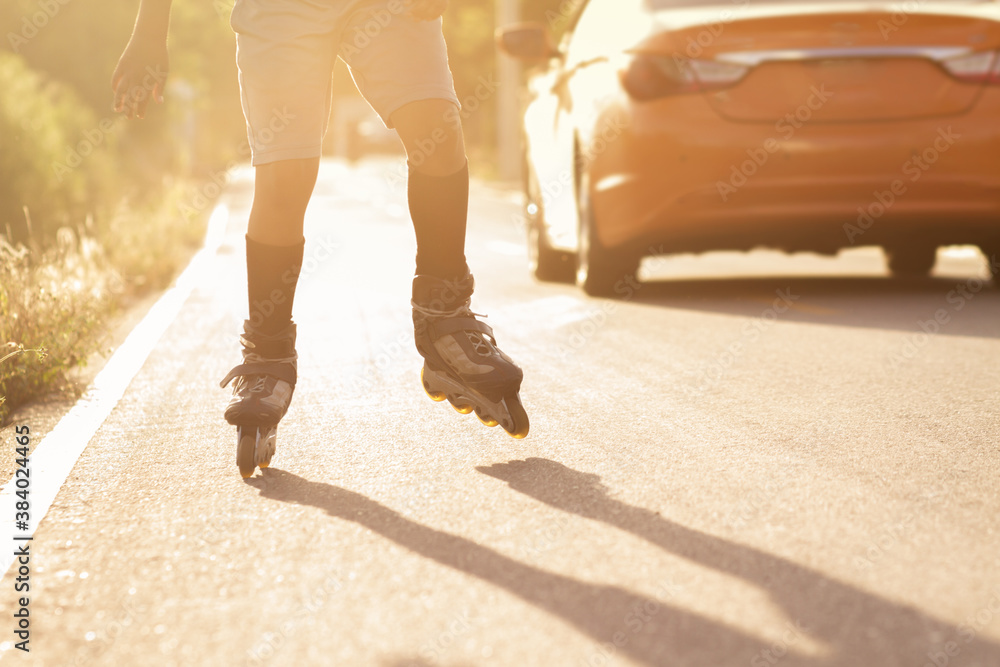 one unrecognizable person skating with rolling skates on a rural paved street ,lower body and back light or sun flare