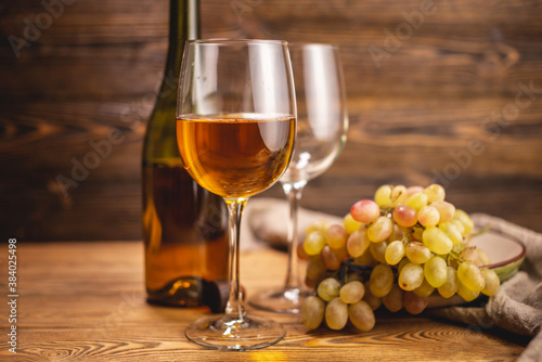 Bottle of dry white wine with a glass and a bunch of grapes on a wooden table. Concept of viticulture and winemaking