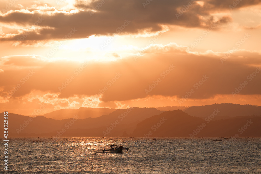 Lonely boat in the ocean by unset with mountains in the horizon. Sunset Over Lombok Island, Indonesia Lonely boat in the ocean by unset with mountains in the horizon. Sunset Over Lombok Island, Indonesia