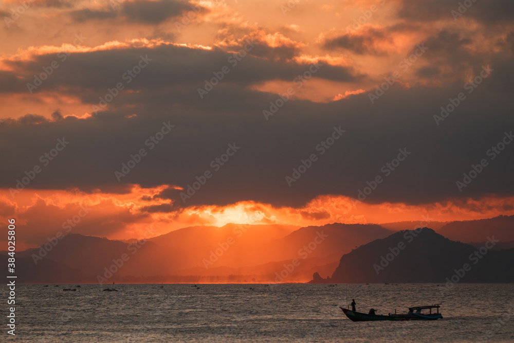 Lonely boat in the ocean by unset with mountains in the horizon. Sunset Over Lombok Island, Indonesia Lonely boat in the ocean by unset with mountains in the horizon. Sunset Over Lombok Island, Indonesia