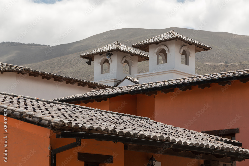 approach to the infrastructure of an old house with a tile roof, in the background a mountain and sky with clouds