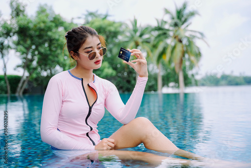 Asian woman traveler in swim suit hold a credit card at swimming pool outdoors.