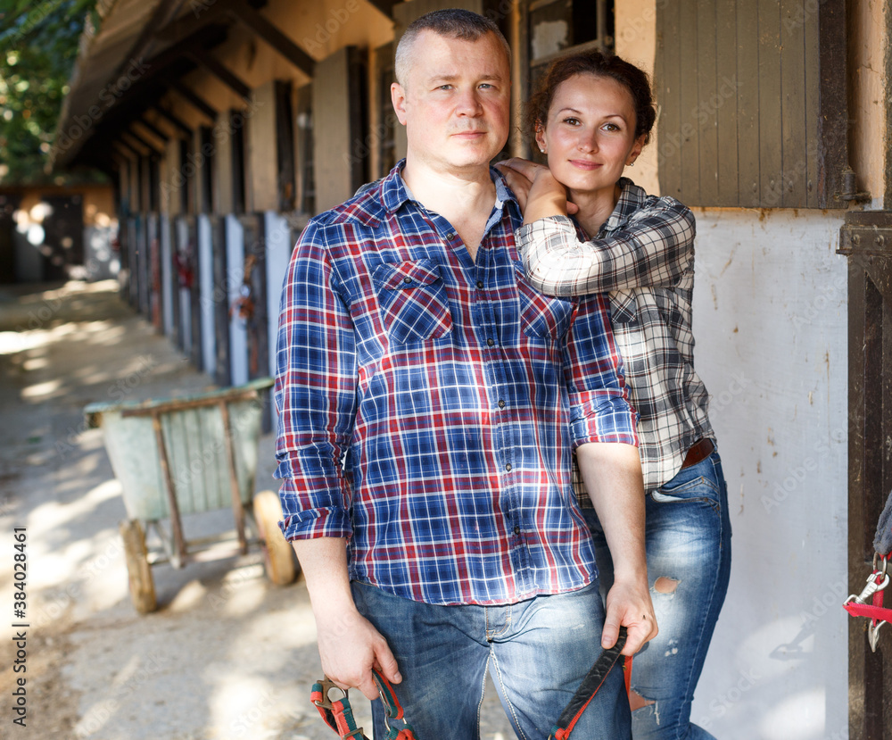 Mature positive family couple with belly-band standing at stable outdoor