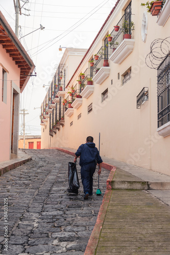 Man doing cleaning of cobbled street of colonial city - man picking up garbage with a bag and broom in street of the historic center of Quetzaltenango Guatemala