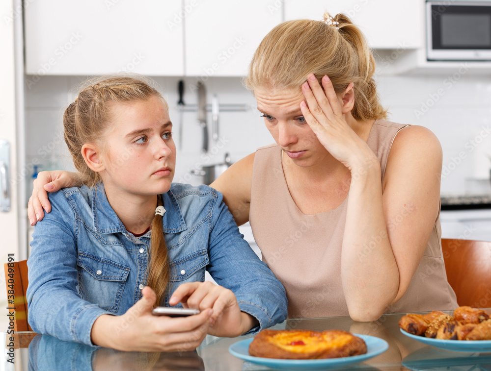 Woman outraged when looking into mobile phone of her teenage daughter at kitchen table